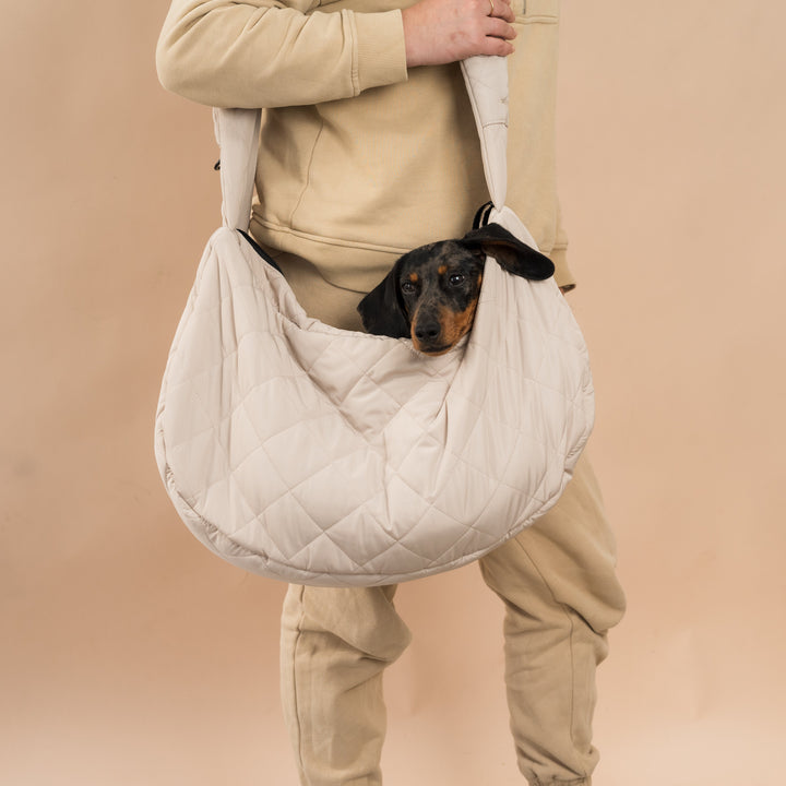 persona con bolso bandolera color beix con teckel tumbado comodamente dentro